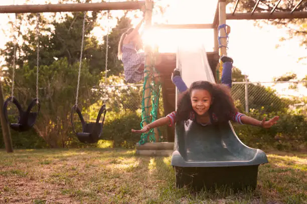 Two Girls Playing Outdoors At Home On Garden Slide