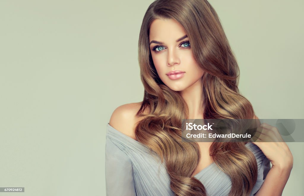 Portrait of gorgeous young woman with elegant make up and perfect hairstyle. Long haired, appealing model with dense, curled, well cared hair. Portrait of gorgeous young woman with elegant make up and perfect hairstyle. Straight look at camera. Beauty Stock Photo
