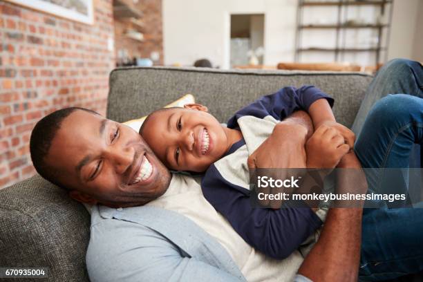 Padre E Hijo Abrazo Juntos En El Sofá Foto de stock y más banco de imágenes de Padre - Padre, Hijo, Abrazar