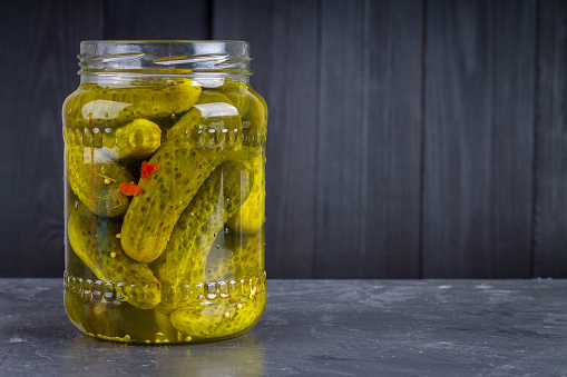 Pickled gherkins or cucumbers in glass jar on a gray background.