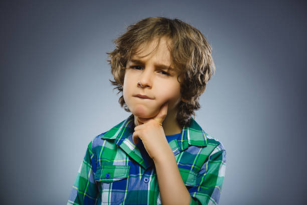 doubt, expression and people concept - boy thinking over gray background stock photo