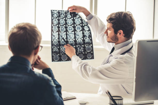At the doctor Handsome young doctor in white coat is showing x-ray image to his patient while working in office brain tumour photos stock pictures, royalty-free photos & images