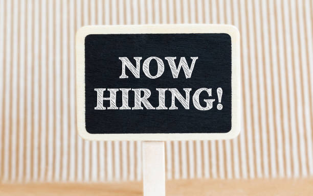 istock Handwritten text Now Hiring with white chalk on a blackboard on a paper background 670979508