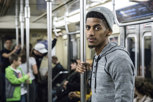 A candid, black man rides a crowded NYC subway train