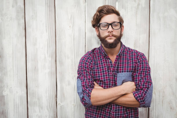 Confident hipster wearing eye glasses with arms crossed standing against wooden wall