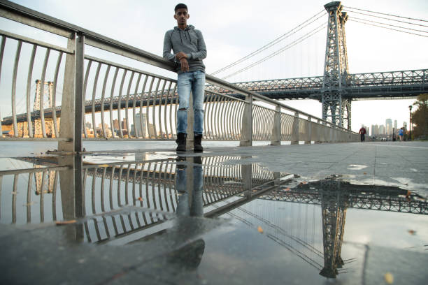 A candid portrait of a young, black man in front of NYC's Williamsburg Bridge at sunset