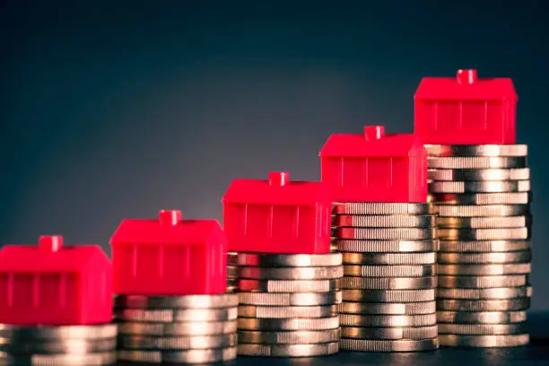 Small red houses stand on stacks of coins.