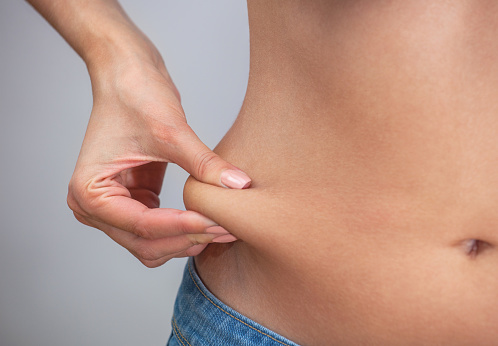 Girl pulls hand the skin on the abdomen, showing the body fat in the abdominal area and sides. Treatment and disposal of excess weight, the deposition of subcutaneous fat.