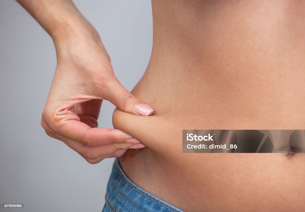 Girl pulls hand the skin on the abdomen, showing the body fat in the abdominal area and sides Girl pulls hand the skin on the abdomen, showing the body fat in the abdominal area and sides. Treatment and disposal of excess weight, the deposition of subcutaneous fat. Adipose Cell Stock Photo
