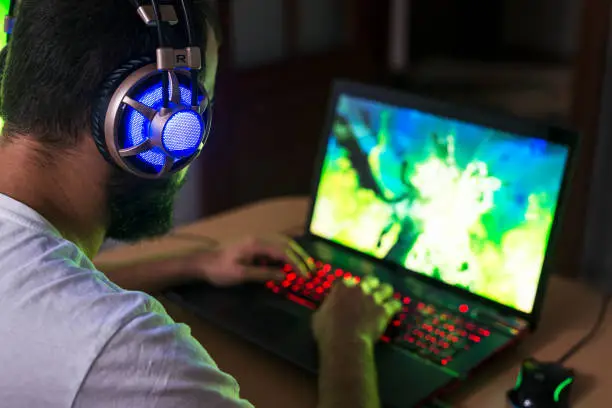 Photo of Young gamer playing video game wearing headphone.