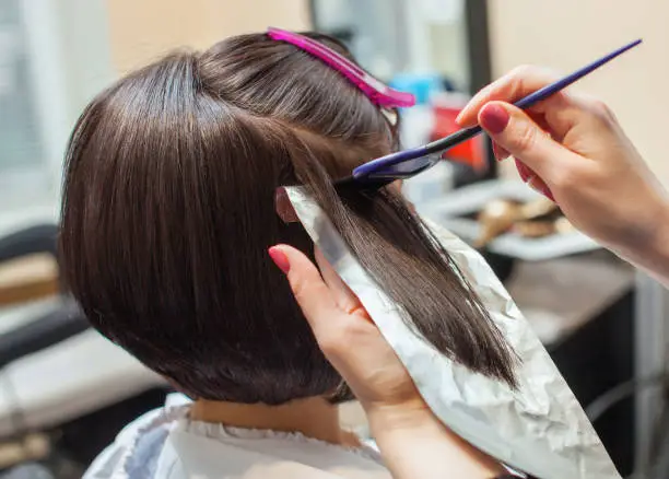 Photo of hairdresser paints the woman's hair in a dark color, apply the paint to her hair