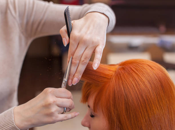 peluquero hace un corte de pelo con tijeras de cabello a un joven con niña de pelo rojo - flequillo fotografías e imágenes de stock