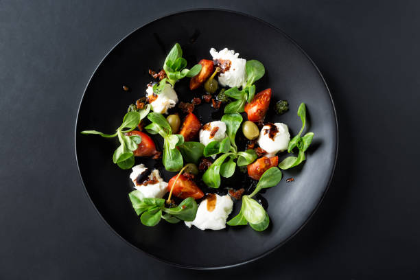 insalata caprese con mozzarella, pomodoro, basilico e aceto balsamico disposta su piatto nero e sfondo scuro. visualizzazione dall'alto - salad food caprese salad gourmet foto e immagini stock