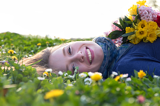 Girl lying on the Green Grass Field and enjoy the flowers. Happiness. Young woman outdoors portrait.