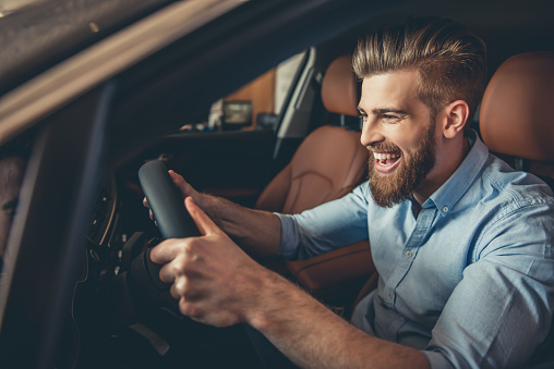 Handsome bearded businessman is smiling while sitting in a new car in car dealership