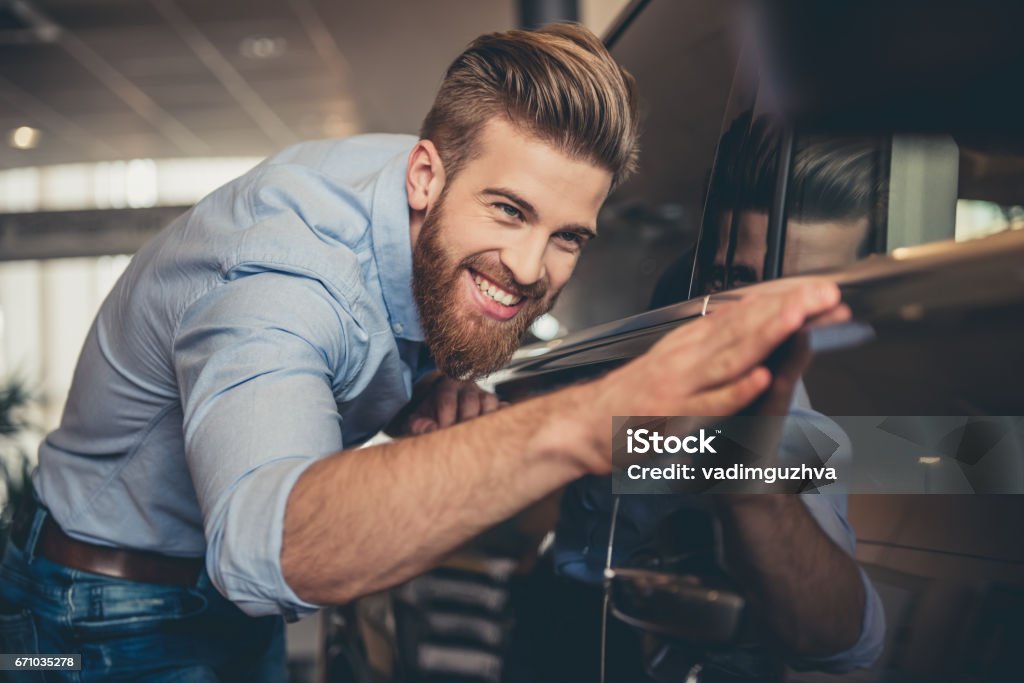 Visiting car dealership Visiting car dealership. Handsome bearded man is stroking his new car and smiling Car Stock Photo