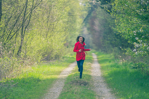 Dark-haired woman in a red coat runs on a path in the forest