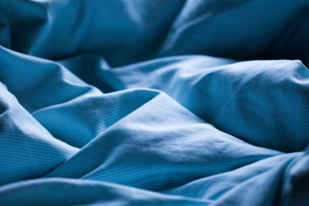 穏やかな朝または夕方のロマンチックな日光の中で穏やかに眠っている青いベッドシーツ - sheet ストックフォトと画像