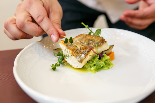 Cook cooks fish dish - baked fillet of pikeperch, zander - hands in frame