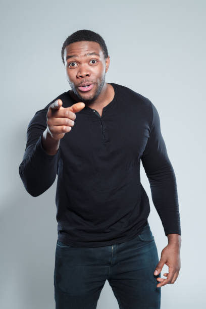 Portrait of excited young african man pointing at camera against gray background