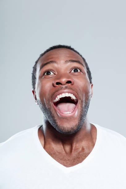 Excited afro american man looking away and laughing Close up portrait of excited young afro american man looking away and laughing against gray background mouth open human face shouting screaming stock pictures, royalty-free photos & images