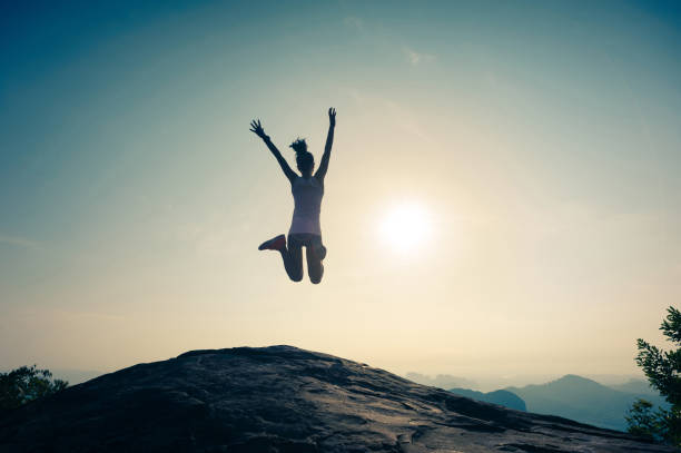 istock cheering successful young woman jumping on mountain peak 671118050