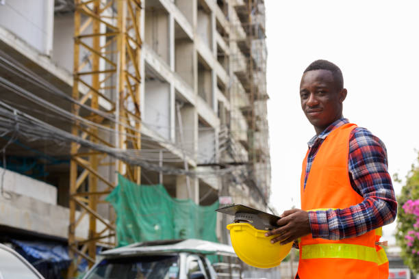 istock Young black African man construction worker holding clipboard and hard hat at building site 671124086