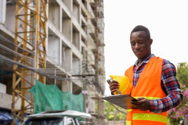 istock Young black African man construction worker reading on clipboard while holding hard hat at building site 671124120