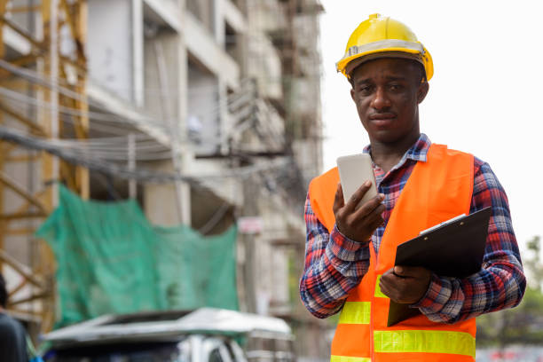 istock Young black African man construction worker holding clipboard and mobile phone at building site 671124216
