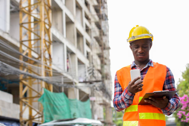 istock Young black African man construction worker reading on clipboard while holding mobile phone at building site 671124298