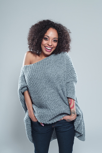 Portrait of beautiful young african woman wearing woolen cardigan and smiling against gray background