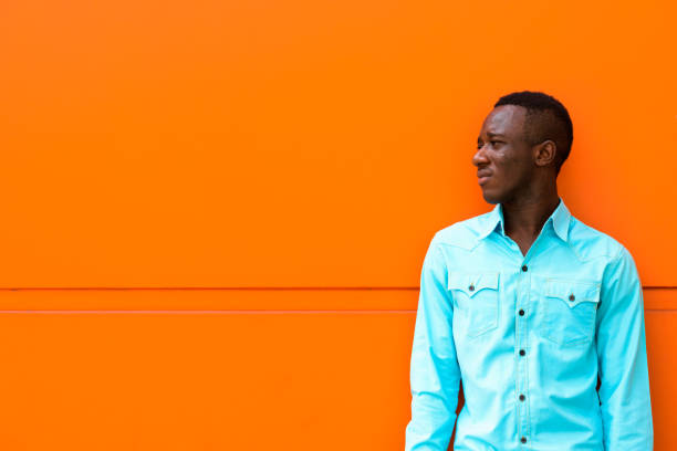 istock Profile view of young black African man thinking while looking at distance against orange painted wall 671124432