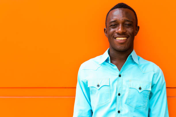 istock Young happy black African man smiling while leaning against orange painted wall 671124490