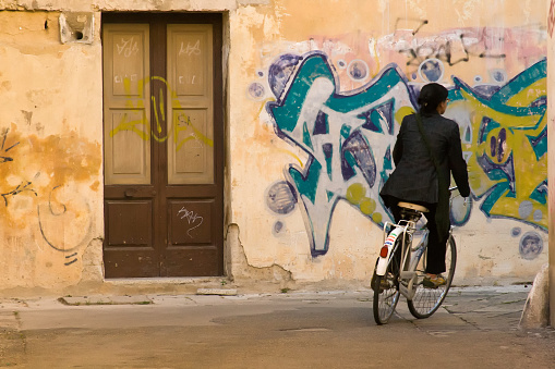 Lecce, Italy: A woman rides a bike past a graffiti-covered wall in the old town of Lecce.