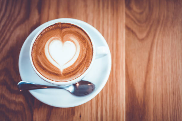 Cappuccino or Latte coffee art cup with heart shaped surface, top view, on wooden table.