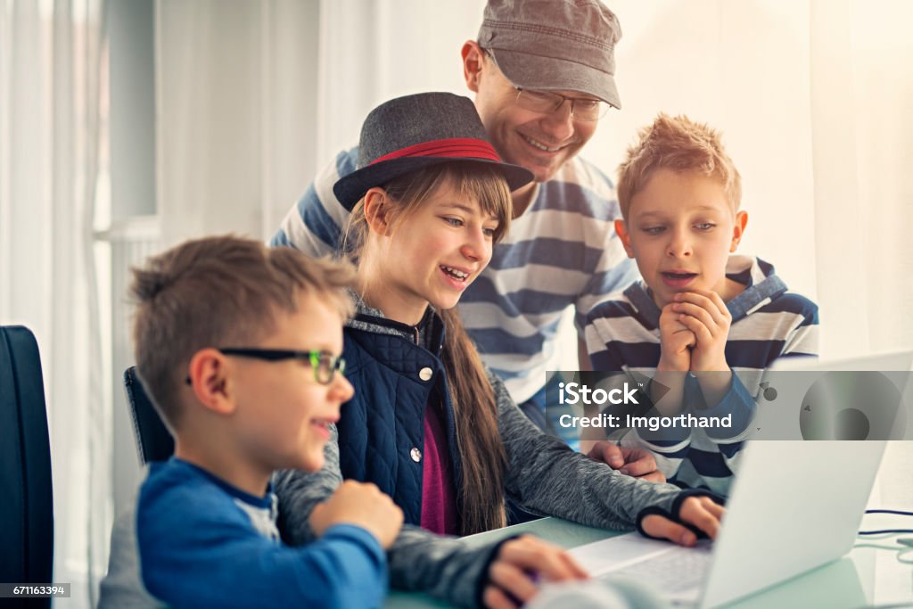 Father having fun coding with kids Father is helping kids in computer science project. The girl aged 11 is using modern ultrabook laptop. Boys aged 7 are curiously looking at the project. 10-11 Years Stock Photo