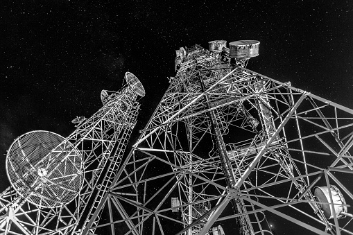 Telecommunication towers for mobile communications and TV antennas in the starry night with noise and grain,monochrome color tone.