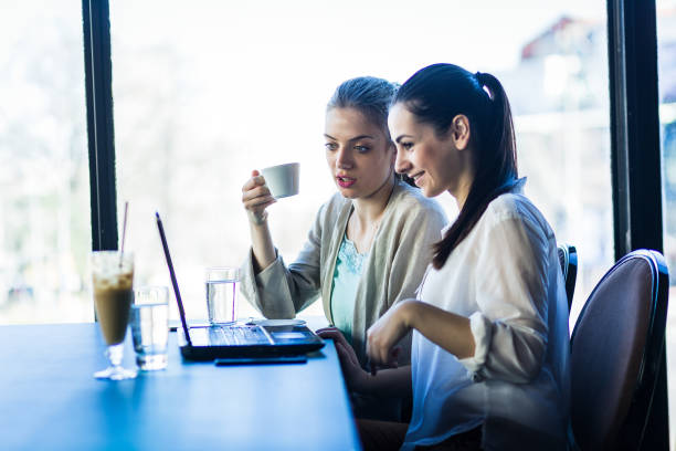 istock Young women drinking coffee and talking at cafe, working on laptop, browsing internet 671179204