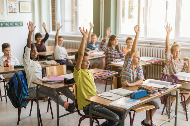 istock Group of elementary students with raised arms in the classroom. 671180160