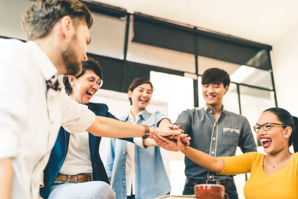 Multiethnic diverse group of happy colleagues join hands together. Creative team, casual business coworker, or college students in project meeting at modern office. Startup or teamwork concept stock photo