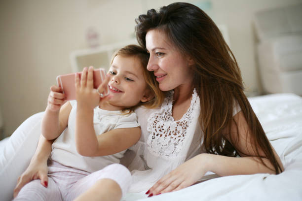istock Smiling mother with daughter using smart phone on bed. 671203452