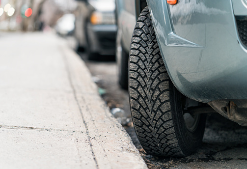 Close-up of a car parked on a hill, with the tire turned into the curb to stop  the car from rolling forward.
