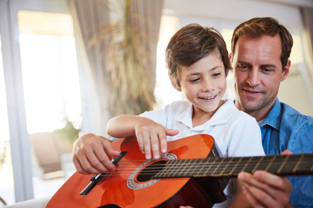 Sharing a love of music with his son Shot of a father and his young son sitting together in the living room at home playing guitar father and son guitar stock pictures, royalty-free photos & images
