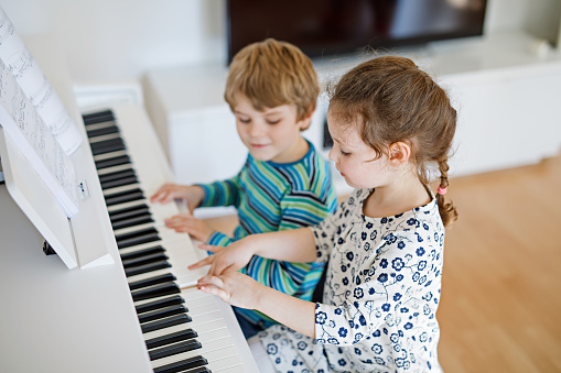 Two little kids girl and boy playing piano in living room or music school. Preschool children having fun with learning to play music instrument. Education, skills concept.