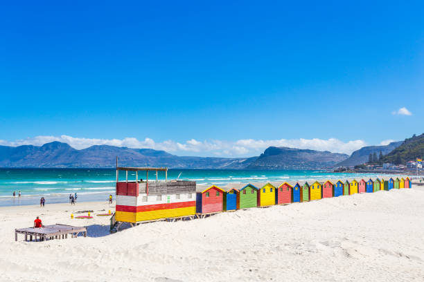 This is a picture of colorful shacks in Muizenberg Beach, Cape Town, South Africa. The contrast with the white sand and the multi-color houses and the blue ocean is amazing.