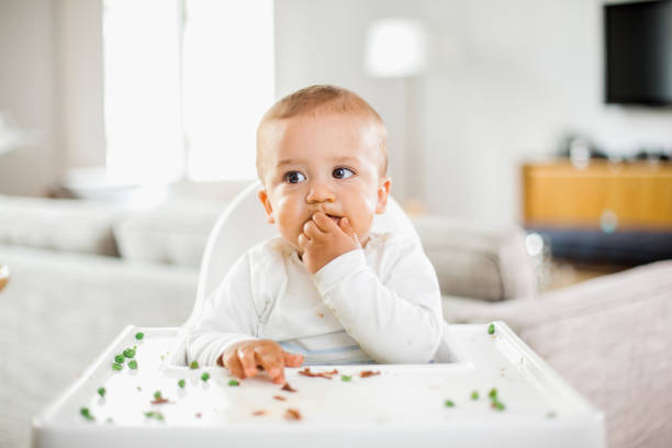 Baby boy eating green peas Baby boy eating green peas high chair stock pictures, royalty-free photos & images