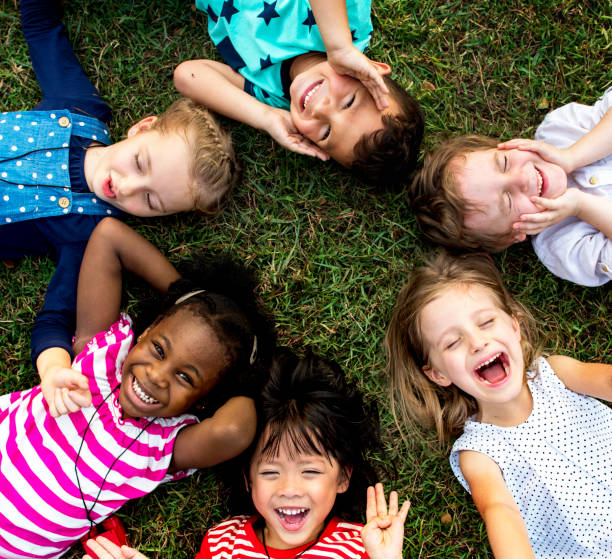 gruppe des kindergartens kinder auf dem rasen im park liegen und entspannen sie mit lächeln auf den lippen - kindheit stock-fotos und bilder