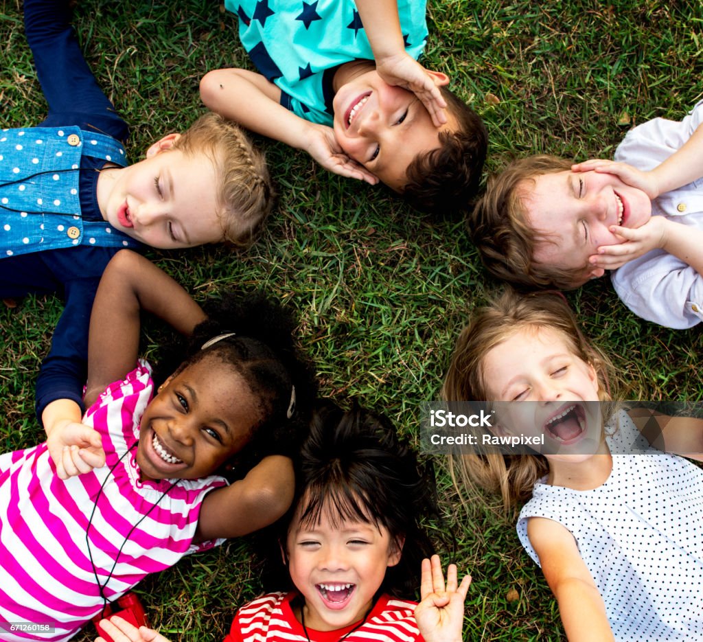 Grupo de niños de jardín de infantes tumbado sobre la hierba en el parque y relajarse con sonrisa - Foto de stock de Niño libre de derechos