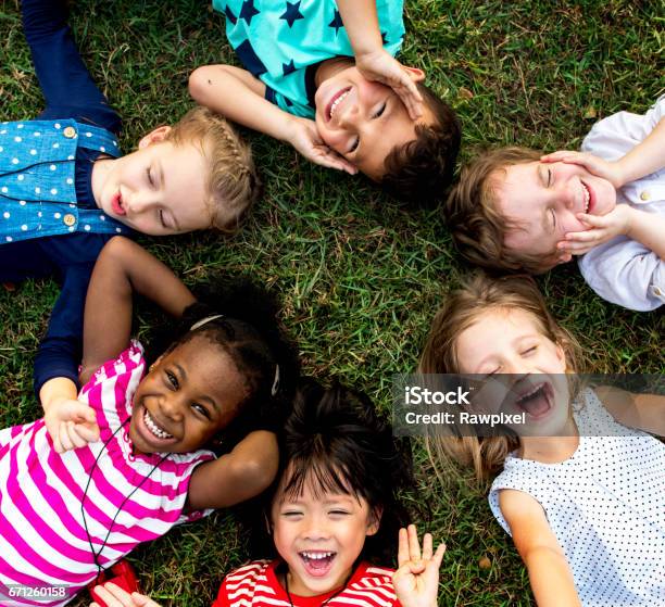 Group Of Kindergarten Kids Lying On The Grass At Park And Relax With Smiling Stock Photo - Download Image Now