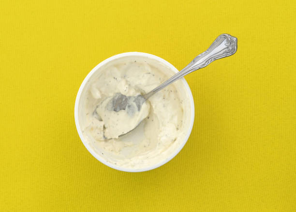 Top view of an opened container of fresh French onion dip with a spoon in the food atop a bright yellow tablecloth.